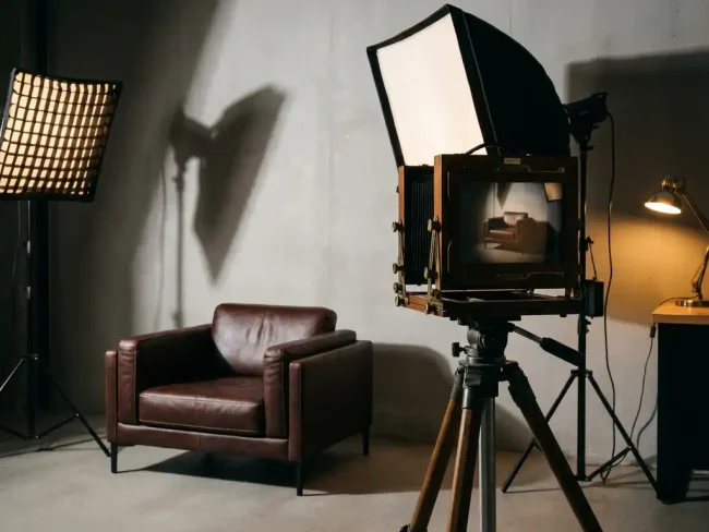 Modern leather armchair with detailed stitching next to vintage camera on tripod in minimalist photography studio