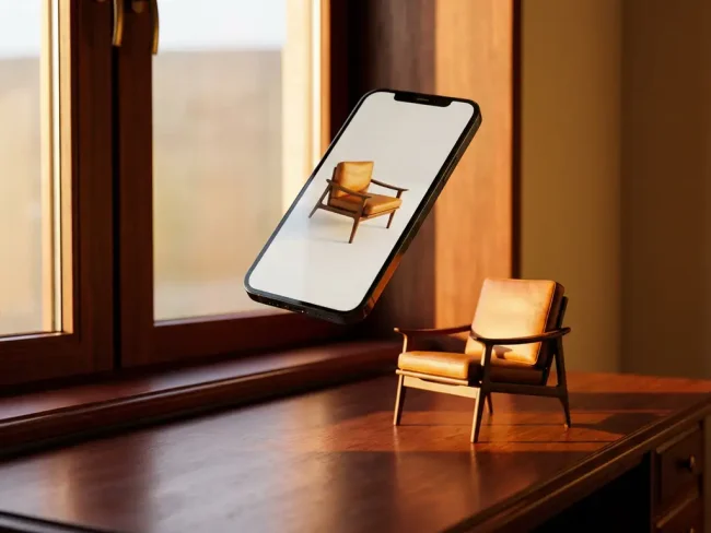 Smartphone displaying 3D furniture model hovers above wooden desk with matching physical chair in warm golden hour lighting